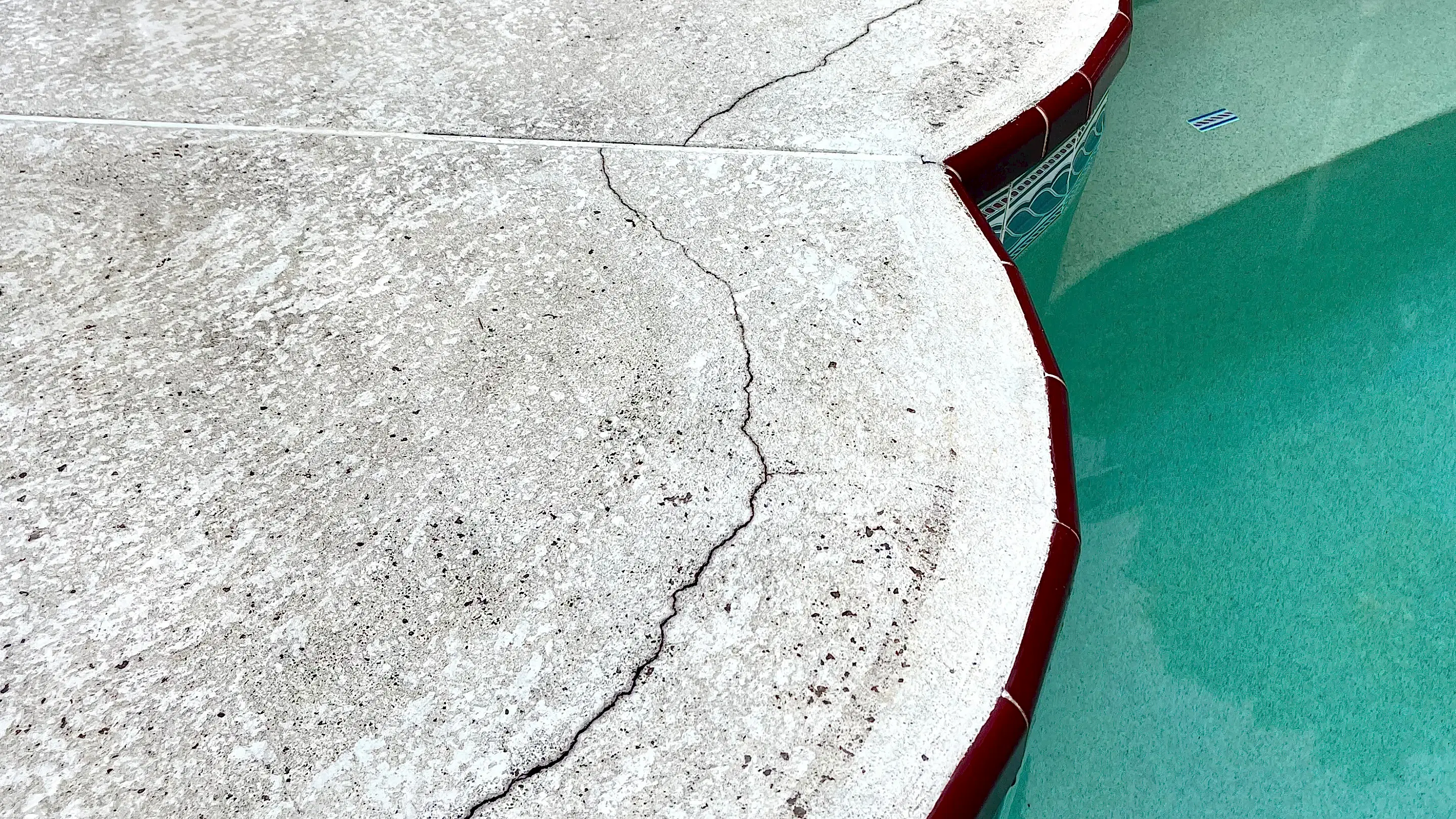 Crack in concrete along an in-ground pool.