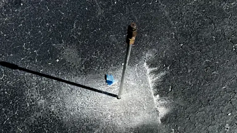 417residential-chemicalgroutpoint Metal probe inserted into cracked asphalt with light debris around the hole, used for measuring ground conditions.