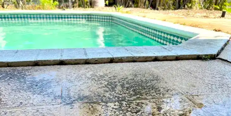430Pool Foundation Stabilization - Unlevel Pool Deck Close view of an unlevel pool deck showing worn concrete and water damage along the edge of a residential swimming pool.