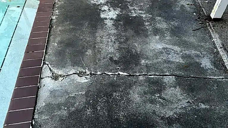 5.1residential-largecrackalongdeck Residential concrete pool deck with a large horizontal crack and surface deterioration next to brick coping and swimming pool.